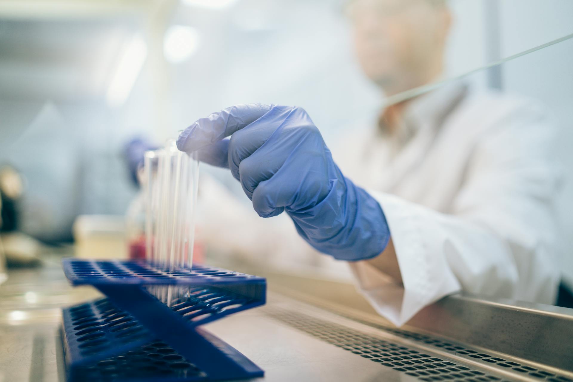 Scientist with blue gloves handling test tubes in a laboratory.