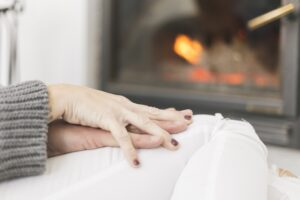 Close-up of hands resting on someone's knee near a cozy fireplace.