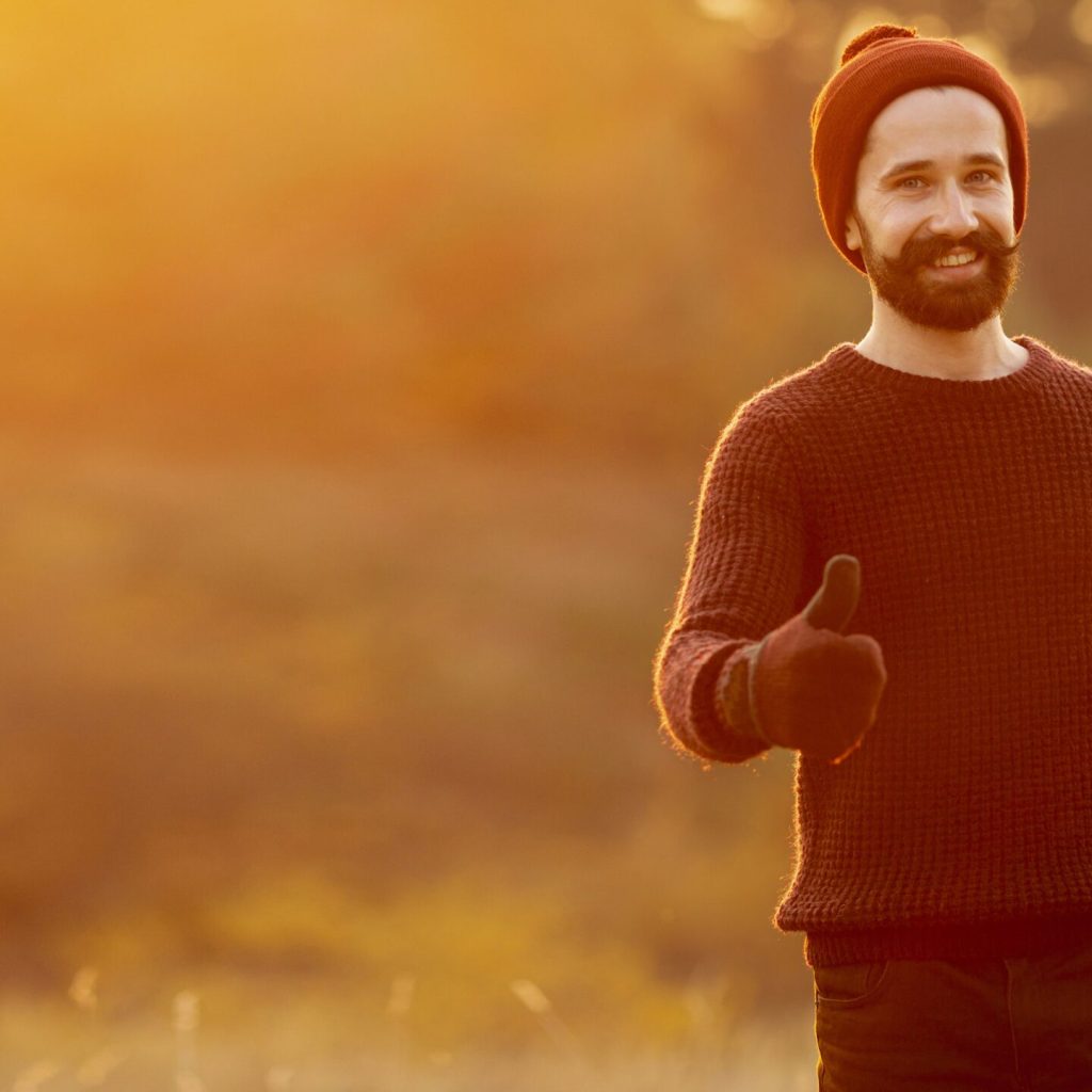 menhealth-2 Smiling man in warm clothes giving a thumbs-up during sunset, symbolizing positivity and men's health